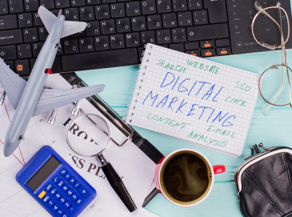Digital marketing on notepad and various office supplies. Flat lay composition with keyboard, coffee and other office related objects on blue background.