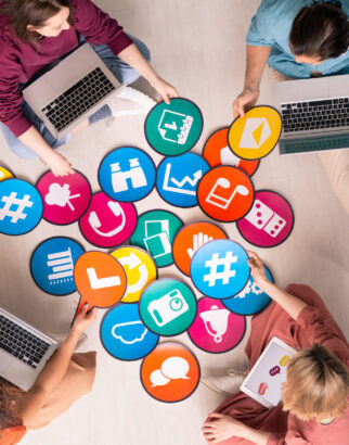 Group of friendly intercultural millennials with mobile gadgets discussing social networks icons on papers while sitting on the floor