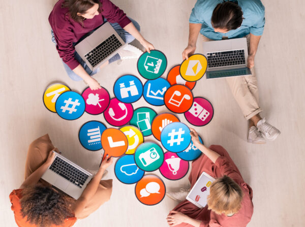 Group of friendly intercultural millennials with mobile gadgets discussing social networks icons on papers while sitting on the floor